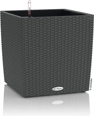 A dark gray, square planter with a woven texture sits on a reflective white surface.