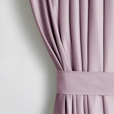 A close-up of a pink/purple velvet curtain with pleats and a tie-back.
