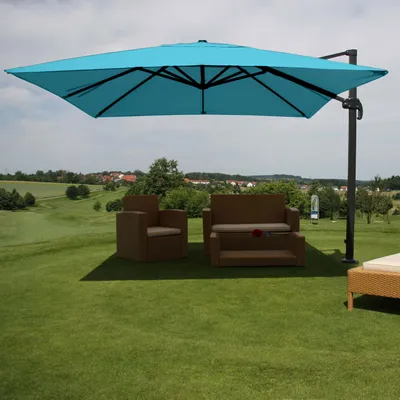 An outdoor patio set with a large turquoise umbrella is set up on a grassy lawn, with a golf course and houses in the background.