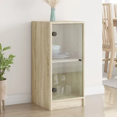 A wooden cabinet with glass doors is shown in a room with a plant and a chair in the background.