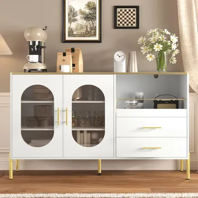 A white sideboard with glass doors and drawers, decorated with golden accents, is shown in a room setting.