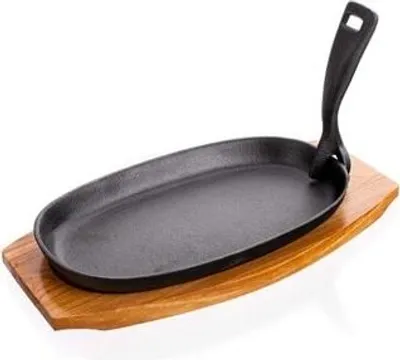 A cast iron oval griddle pan with a black handle, placed on a wooden board.