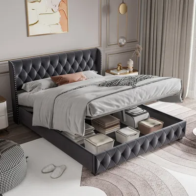 A tufted upholstered bed frame with the storage drawers open, revealing storage bins and stacked items inside. The bed is made up with bedding and a decorative pillow.