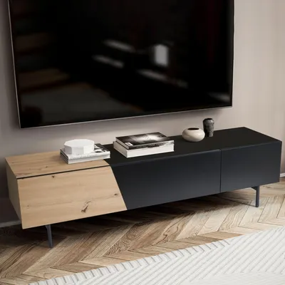 A modern TV stand with a black and wood finish, placed on a wooden floor in front of a wall with a large TV mounted above it.