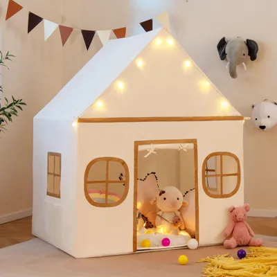 A white playhouse tent for children, decorated with string lights and featuring stuffed animals and colorful balls inside and around it.