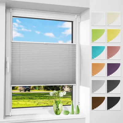 A window with a gray pleated blind, showing a view of a grassy field and blue sky with clouds. Decorative green vases and a green apple are on the windowsill.