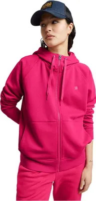 A woman wearing a pink hooded jacket and pink pants, also wearing a blue baseball cap.