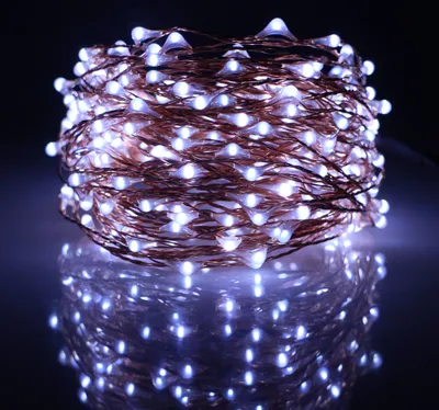 A coiled string of white LED lights with copper wire, reflected on a dark surface.