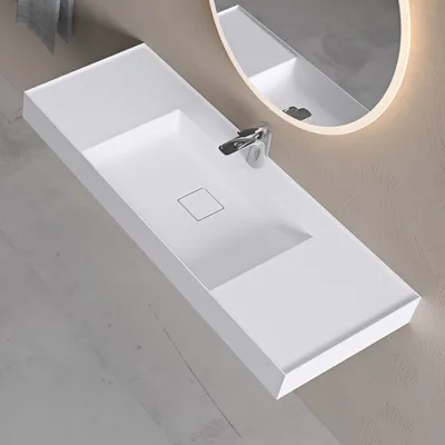 A modern white washbasin mounted on a wall with a faucet and a mirror in the background.