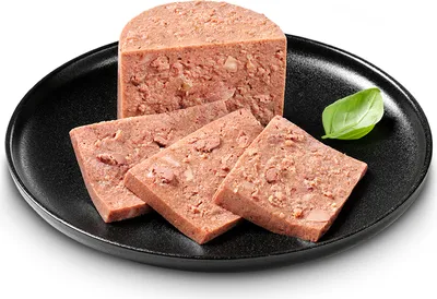 A block of corned beef, sliced, on a black plate with a basil leaf.