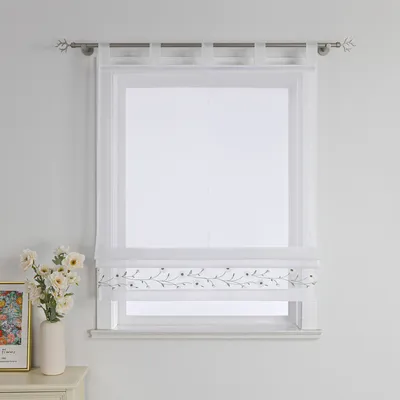 A white sheer Roman blind with a floral embroidered border hangs on a window.