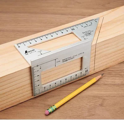 A metal combination square is placed on a wooden beam, with a pencil nearby, indicating its use in woodworking or construction.