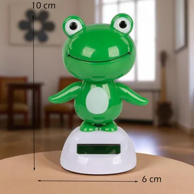 A solar-powered wackelfigur frog toy is displayed on a table in a room.