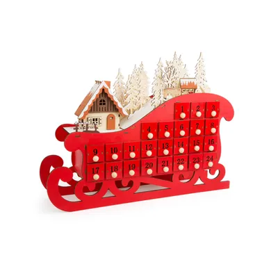 A red wooden advent calendar shaped like a sleigh, decorated with a small house and trees.