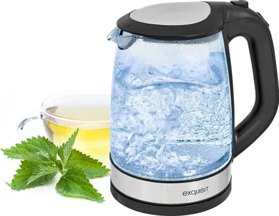 A glass electric kettle with boiling water, a cup of tea, and mint leaves.