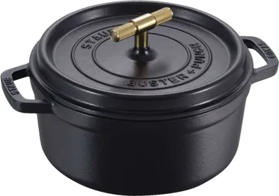 A black Staub cast iron pot with a gold handle is shown against a white background.