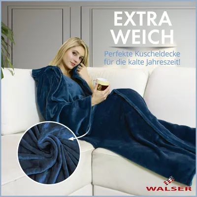 A woman is sitting on a couch wrapped in a blue blanket with sleeves, holding a mug.