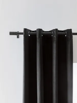 A close-up view of a black curtain hanging from a curtain rod against a white wall.