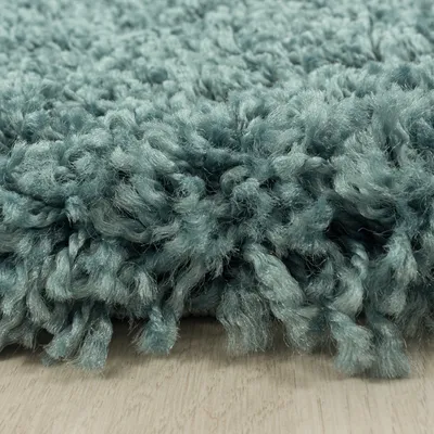 A close-up view of a shaggy teal rug with a light wooden floor visible underneath.