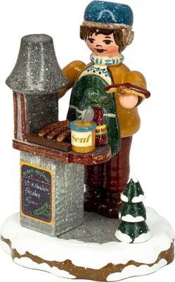 Ein fröhlicher Junge in winterlicher Kleidung steht an einem kleinen Bratwurststand mit einem Tablett voller Würstchen und einem Senfglas während ein kleiner Tannenbaum den verschneiten Boden schmückt