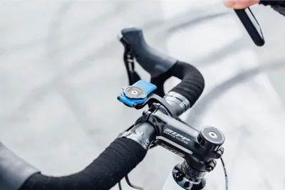 A close-up shot of a blue Quad Lock bike mount attached to the handlebars of a bicycle.