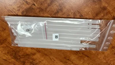 A plastic bag containing several white rods, likely for a blind or curtain, lies on a wooden surface.