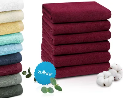 A stack of folded burgundy towels next to a stack of towels in various colors.