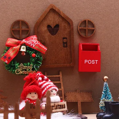 A miniature Christmas-themed scene with a wooden door, wreath, mailbox, ladder, and two elf figures.