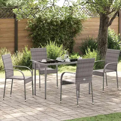 A patio set with four chairs and a table is arranged on a paved patio surrounded by greenery and a wooden fence.