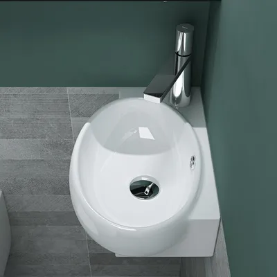 A top-down view of a white ceramic sink with a chrome faucet, set against a teal wall and gray tiled floor.