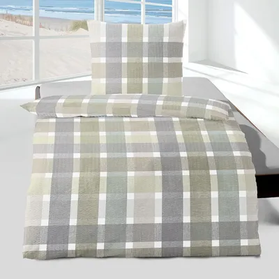 A plaid patterned duvet cover and pillowcase set on a bed, with a window view of a beach in the background.