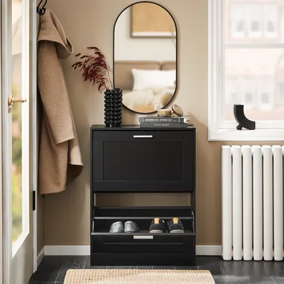 A narrow black shoe cabinet with two flip-down drawers is shown in a hallway next to a door and a window with a radiator.