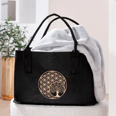 A black felt tote bag with a golden tree and flower of life motif, containing a light gray blanket.