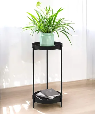 A plant stand with a plant on top and books on the bottom shelf, placed indoors.