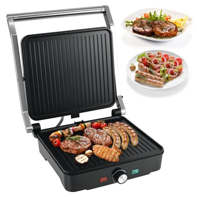 A black and silver electric grill with food on it, and two plates of food in the background.