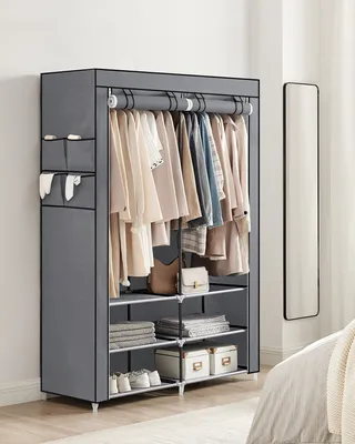 A grey fabric wardrobe with clothes hanging inside and shelves below, placed in a room.
