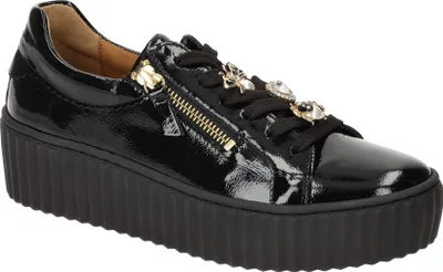 A black patent leather sneaker with a platform sole and decorative embellishments on the laces.