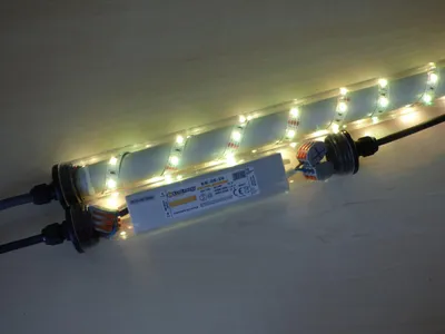 A close-up view of an LED light strip with a power supply unit attached, mounted on a wooden surface.