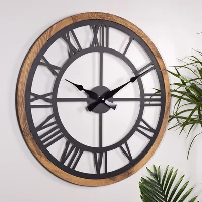 A large, round wall clock with a wooden frame and black metal Roman numerals and hands, mounted on a white wall.