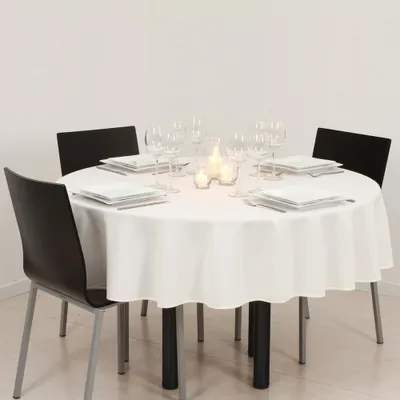 A round table set for a meal with white tablecloth, plates, glasses, and candles.