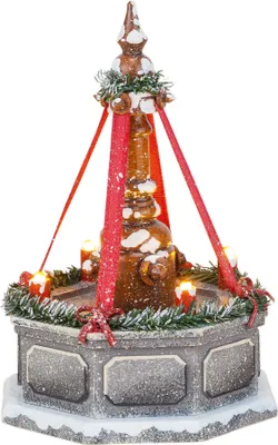 A festive, snow-dusted Christmas decoration resembling a fountain or monument, with red ribbons and lit candles.