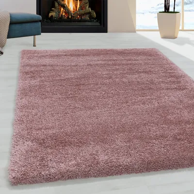 A pink shaggy rug is laid out on a light-colored wooden floor in front of a fireplace.