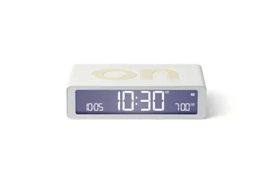 A white digital alarm clock with a gray display is shown against a white background.