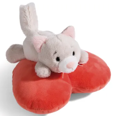 A plush cat toy lying on a red heart-shaped pillow.