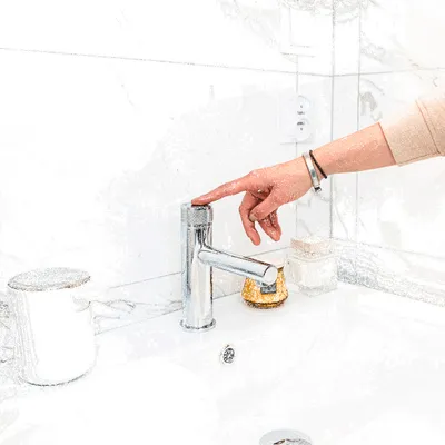 A hand is shown turning on a faucet in a modern bathroom.