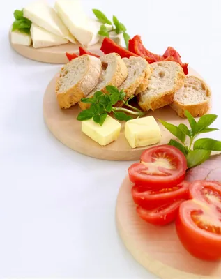 A food platter with cheese, bread, tomatoes, and herbs on wooden boards.