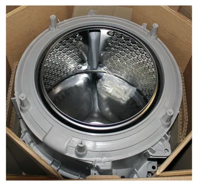 A washing machine drum and outer casing are shown inside a cardboard box.