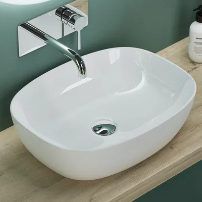 A white ceramic sink with a chrome faucet is shown on a wooden countertop against a teal wall.