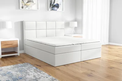 A white boxspring bed with a headboard is shown in a bedroom setting.