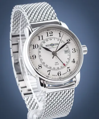 A close-up studio shot of a silver Zeppelin LZ127 Graf Zeppelin watch with a white face and a mesh metal band, set against a blue background.